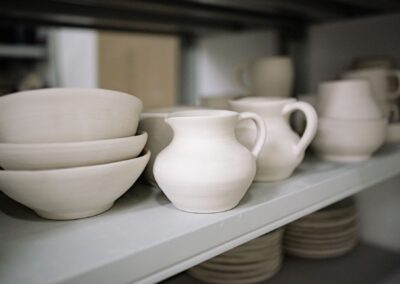 Close-up of handmade pottery bowls and jugs on a workshop shelf, showcasing artisanal craftsmanship.